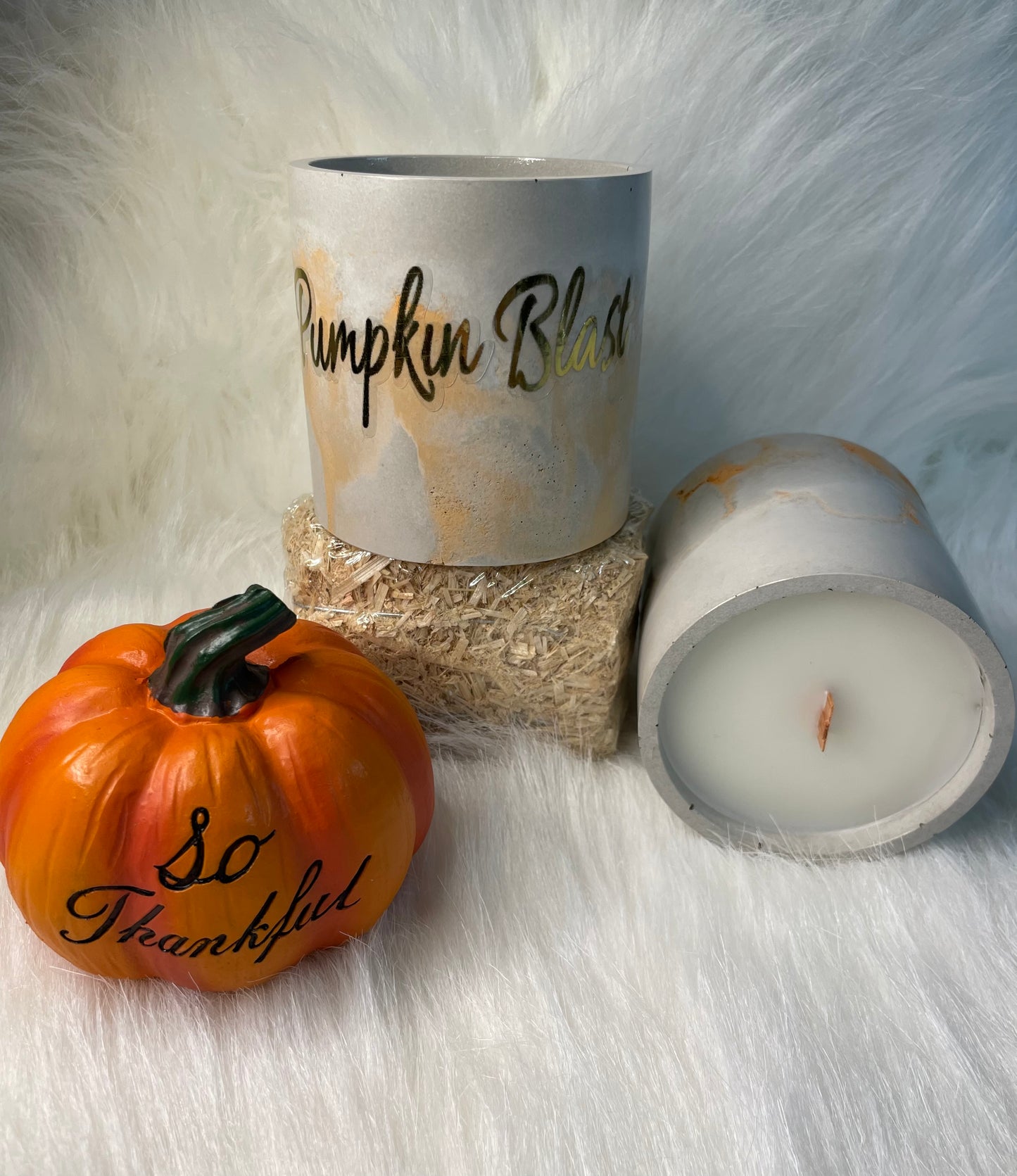 Pumpkin Blast candle in a cement vessel on a hay bin next to a small pumpkin 